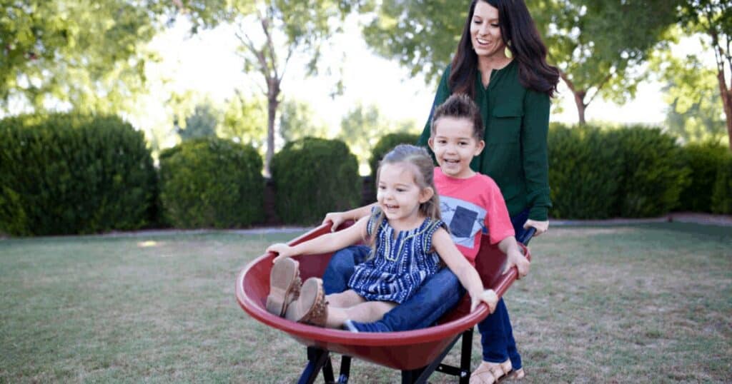 Young mother playing with children outdoors in wheelbarrow