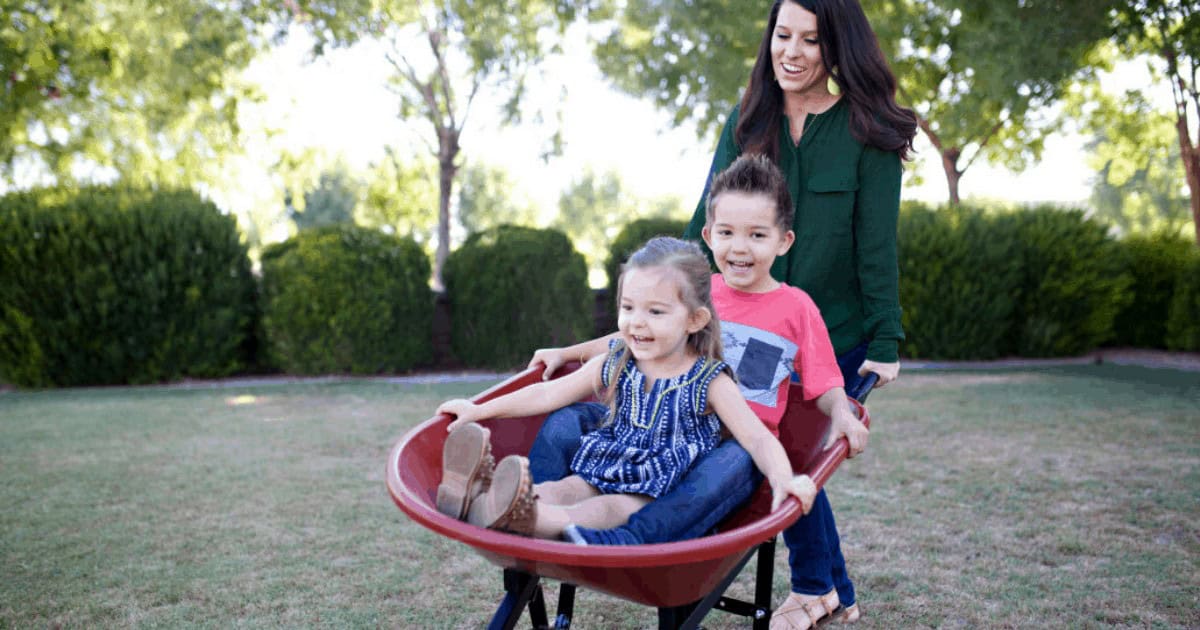 Young mother playing with children outdoors in wheelbarrow
