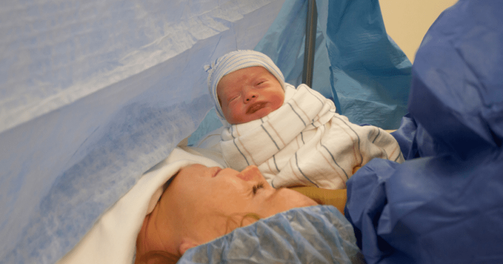 Newborn baby is presented to Mom, on an operating table, during a cesarean birth