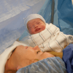 Newborn baby is presented to Mom, on an operating table, during a cesarean birth