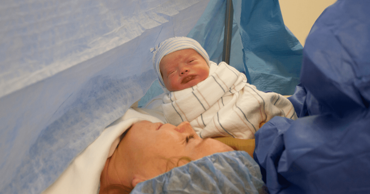 Newborn baby is presented to Mom, on an operating table, during a cesarean birth