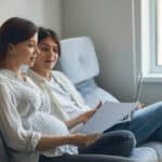 Pregnant couple sitting with a laptop and a postpartum plan
