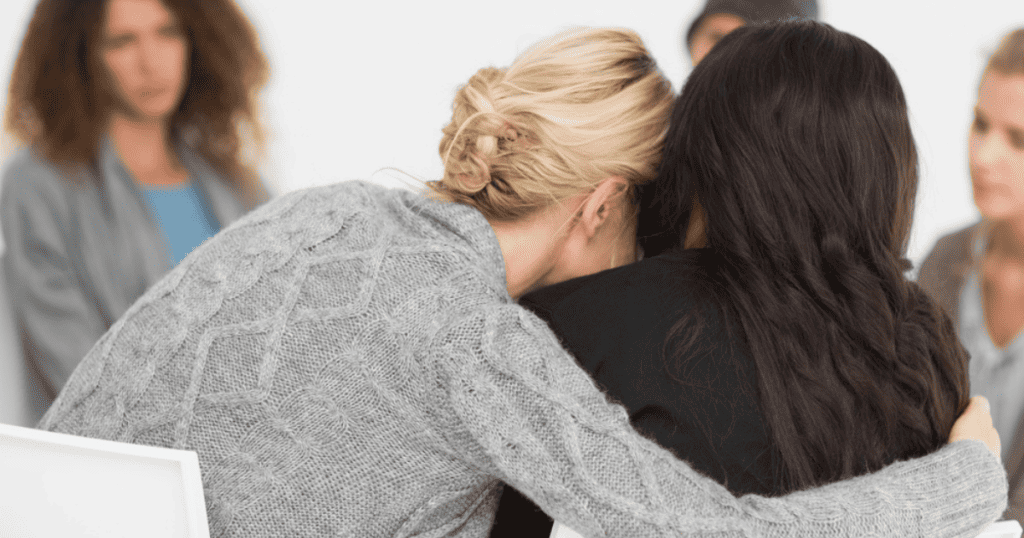 Woman embracing another women in a therapy group, recovering after a traumatic birth experience