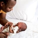 father holding crying infant next to bed