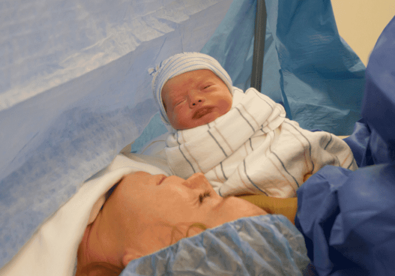 Newborn baby is presented to Mom, on an operating table, during a cesarean birth