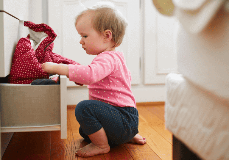 childproofing checklist, baby playing in a drawer in the bedroom