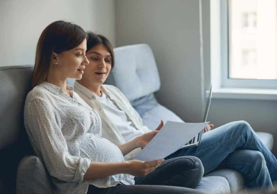 Pregnant couple sitting with a laptop and a postpartum plan