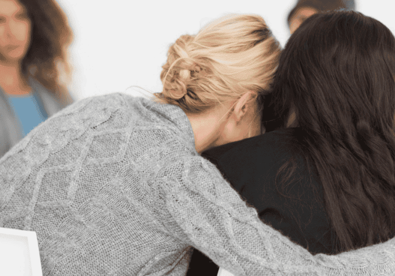 Woman embracing another women in a therapy group, recovering after a traumatic birth experience