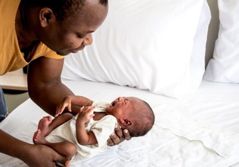 father holding crying infant next to bed