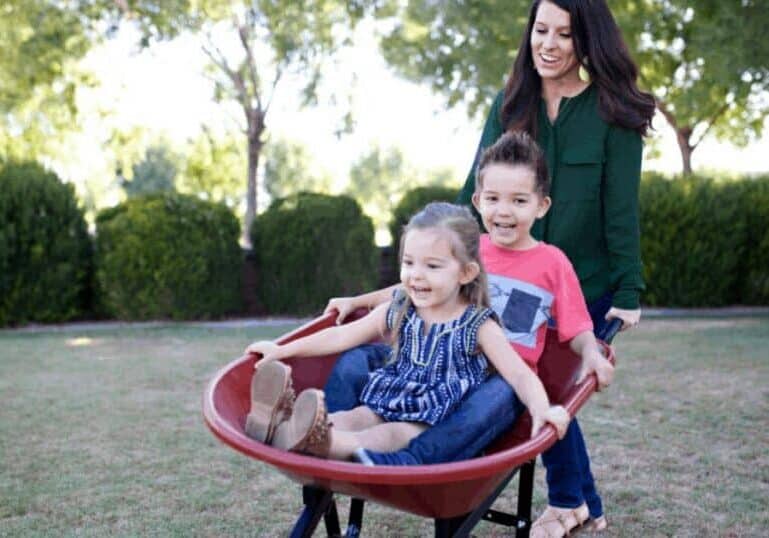 Young mother playing with children outdoors in wheelbarrow